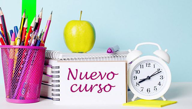 On a light table there are books, stationery, a white alarm clock, an apple. Next to it is a notebook with the text BACK TO SCHOOL. Educational concept.