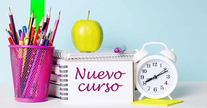 On a light table there are books, stationery, a white alarm clock, an apple. Next to it is a notebook with the text BACK TO SCHOOL. Educational concept.